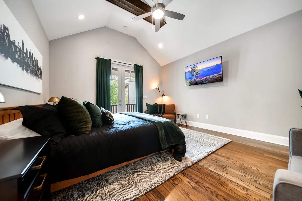 This image features a king-sized bed adorned with plush bedding and decorative pillows, a large window with curtains inviting natural light, a television mounted on the wall, an accent chair, and tasteful artwork. The scene exudes serenity and spacious comfort, suggesting a tranquil retreat ideal for unwinding after a day in the city.