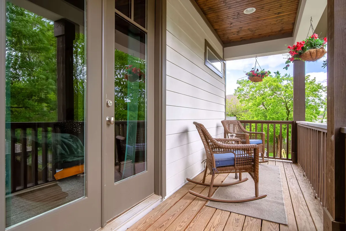 The image showcases a charming exterior porch with wooden rocking chairs, hanging plants, and a sturdy wooden railing. The atmosphere is tranquil and inviting, suggesting a peaceful outdoor space ideal for relaxing or socializing after an energetic night out.
