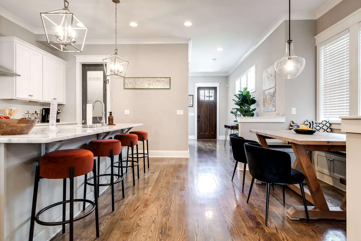 A warm and welcoming kitchen-dining space with a kitchen island, bar stools, a dining table, decorative wall art, and a green plant in the corner. The scene blends kitchen amenities with a stylish dining area for shared meals.
